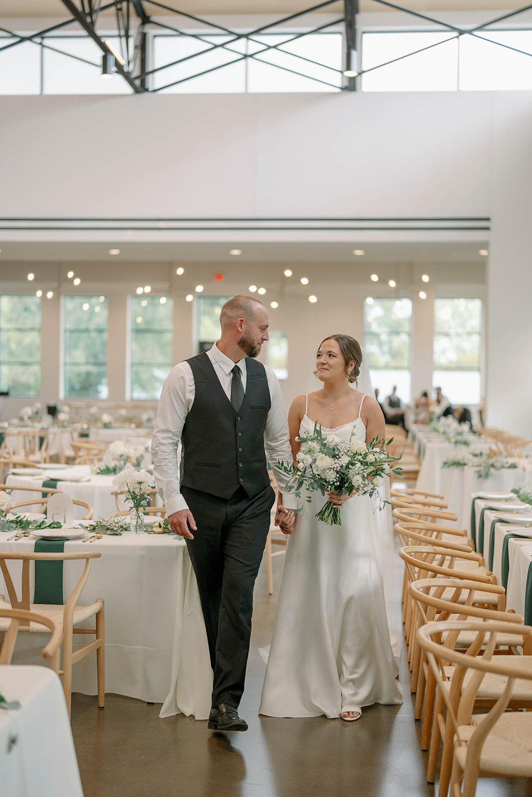 Bride and groom walking hand-in-hand through their beautifully decorated and empty reception space at Leona Road Wedding Venue in Grand Rapids, Michigan.