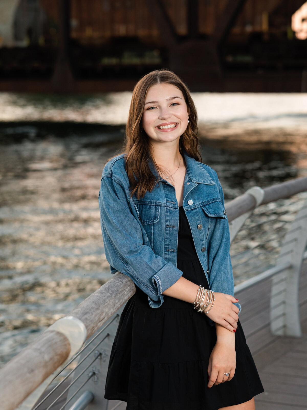 senior girl in jean jacket posed by water for senior portraits