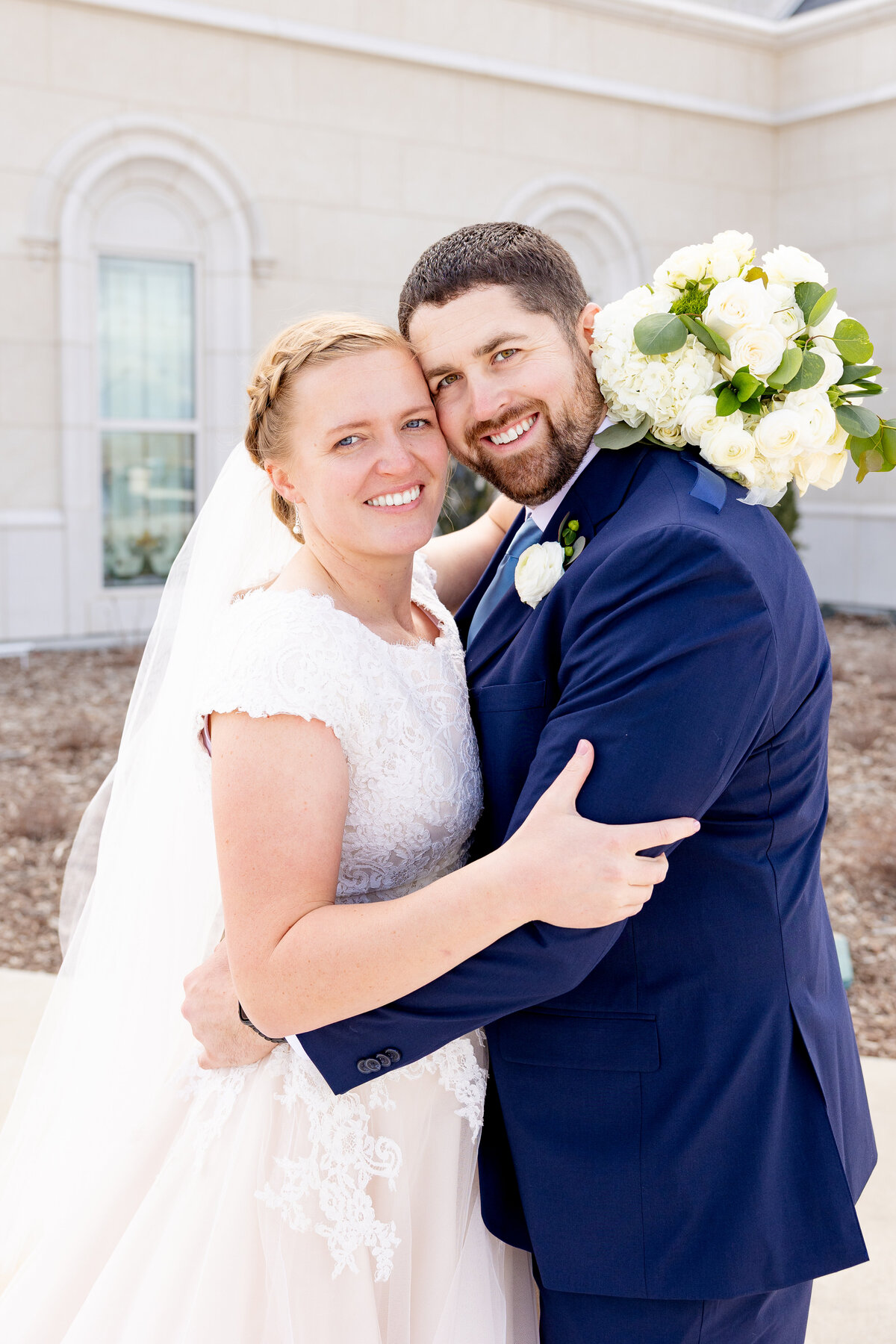 The bride and groom smile as they embrace, the groom holding the bridal bouquet over his shoulder.