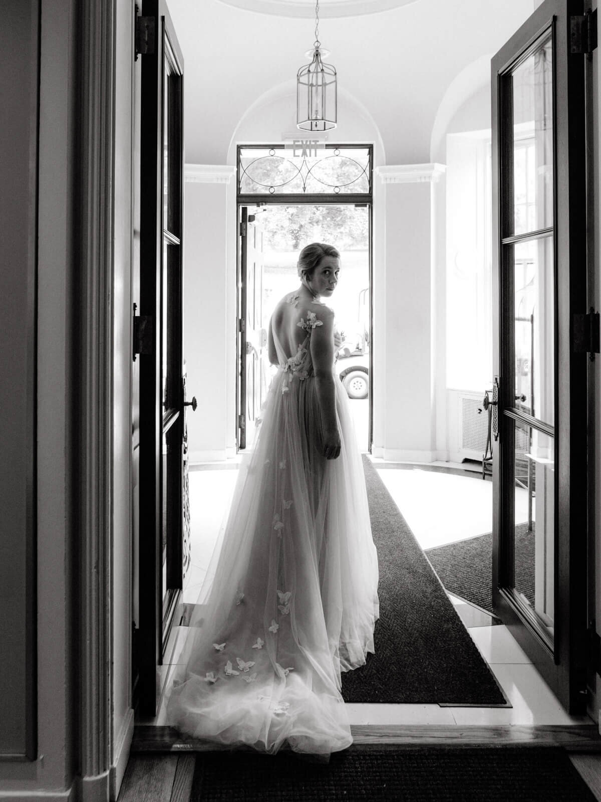 The bride, looking back,  is standing in the middle of large, glass doors.