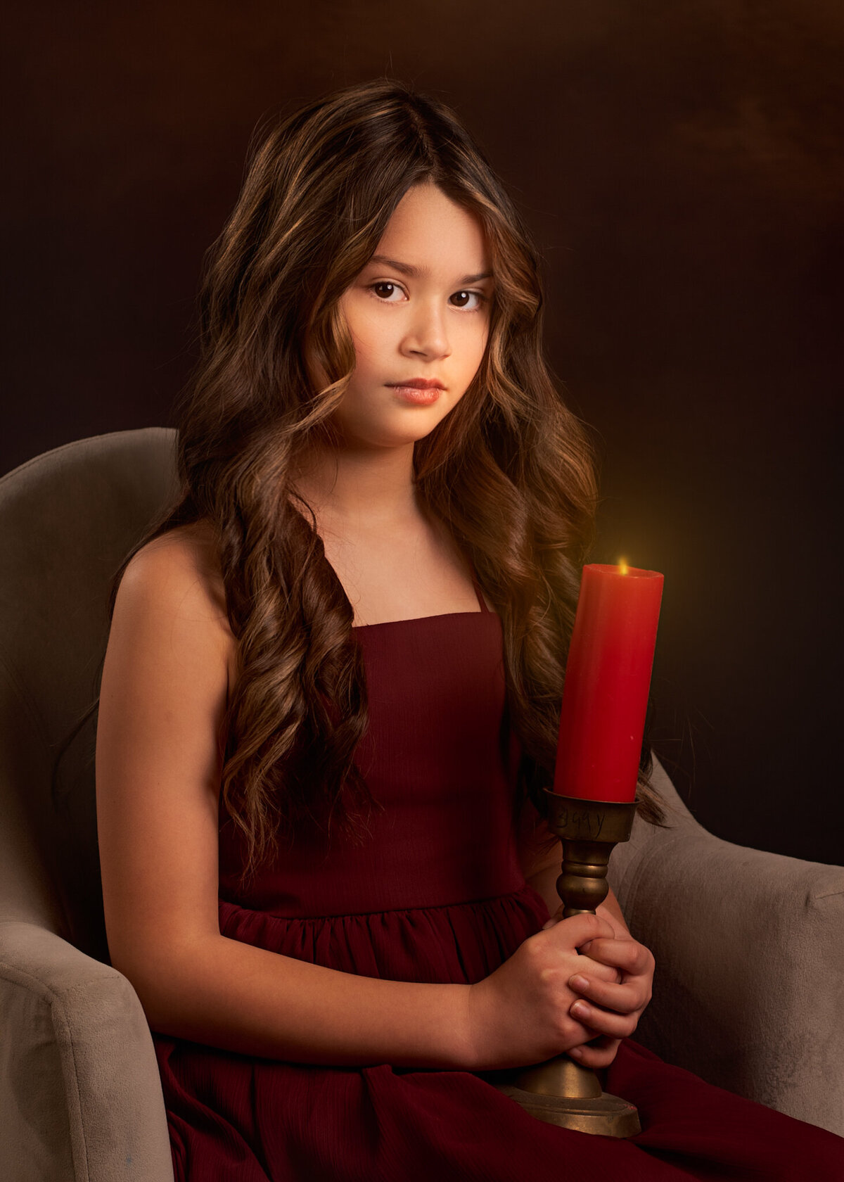 Stunning fine art portrait of a young girl in a deep red dress holding a candle, set against a dramatic dark backdrop. Captured in Overland Park, Kansas, this elegant and artistic setup is perfect for families seeking sophisticated child photography