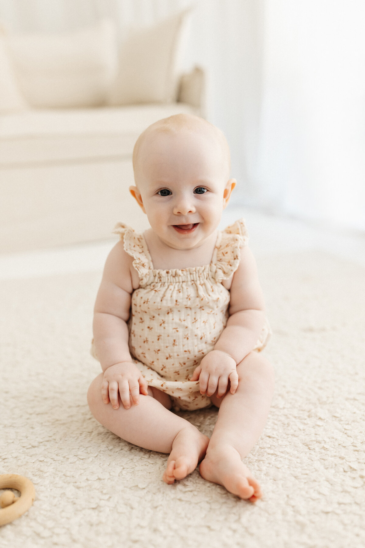 A little girl wearing a floral cream overall and smiling at the camera while she's photographed by lucy jane in her photography studio