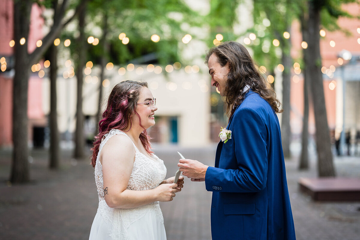 A bride and groom smile widely at one another as they prepare to read their vows on their elopement day in a secluded, private, tea-lit alleyway in Roanoke, Virginia.