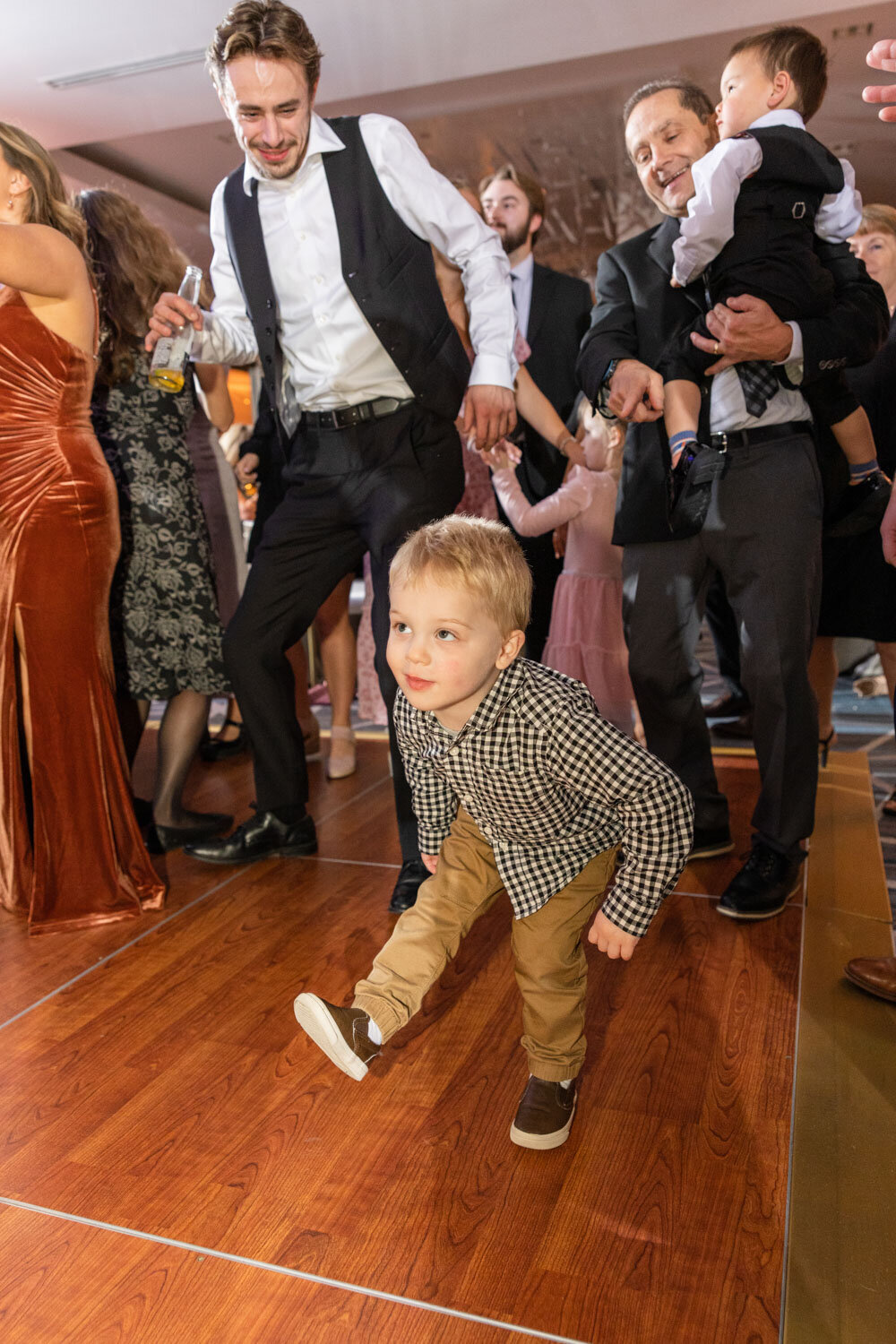 A little boy in a plaid shirt is walking on a wooden floor