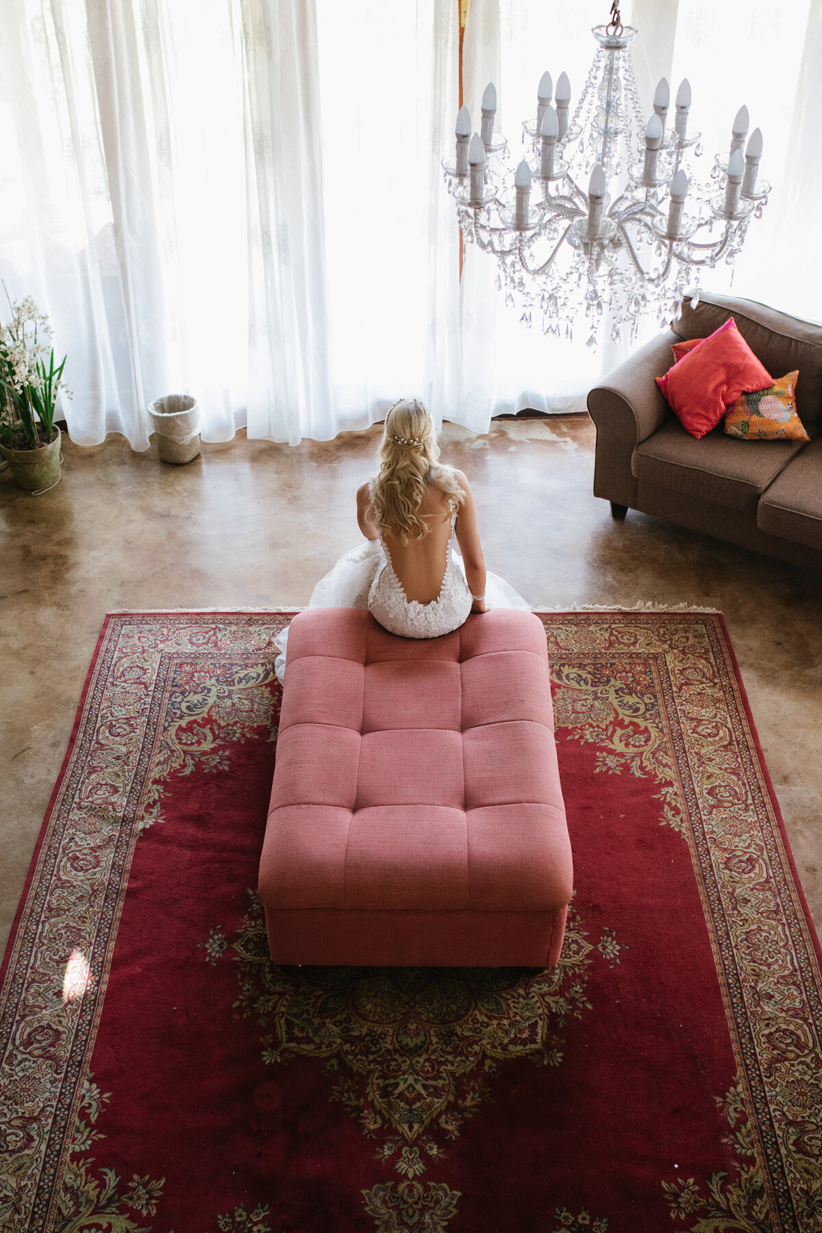 The bride sits on the edge of a red furniture piece moments before she gets married. 