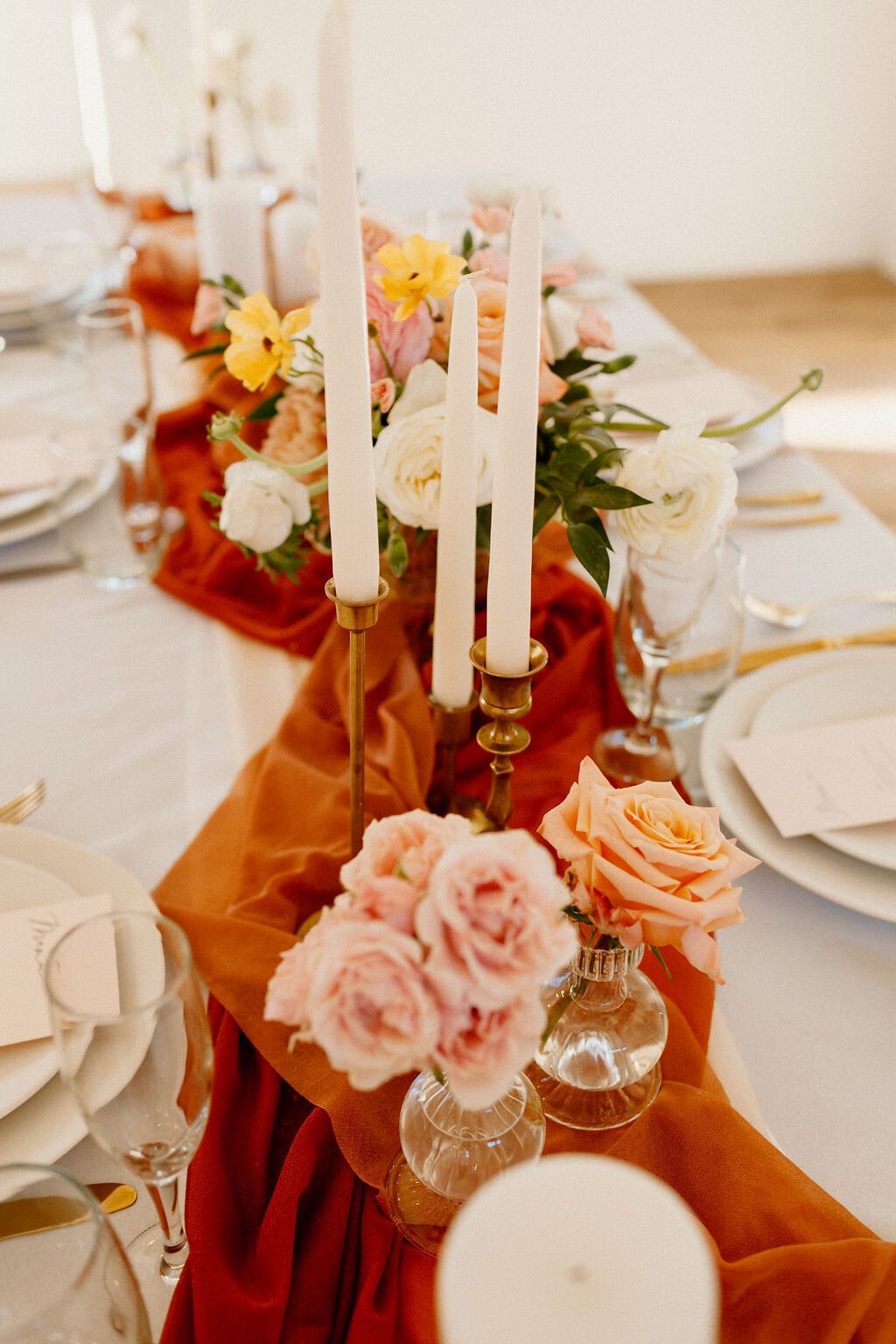 Terracotta table runner with taper candles and roses in glass designer vases at White Aspen Creative in Bend Oregon