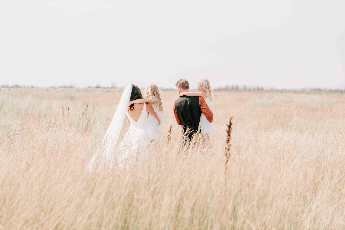 Bride and groom hold their kids and walk away from the camera int he field. 