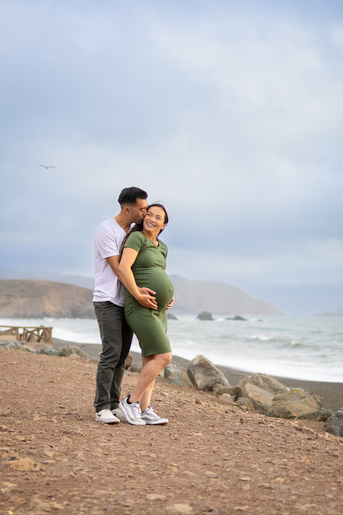 Bay Area Maternity Portfolio - Ellobelle Photography with romantic ocean-side maternity portrait as dad kisses mom