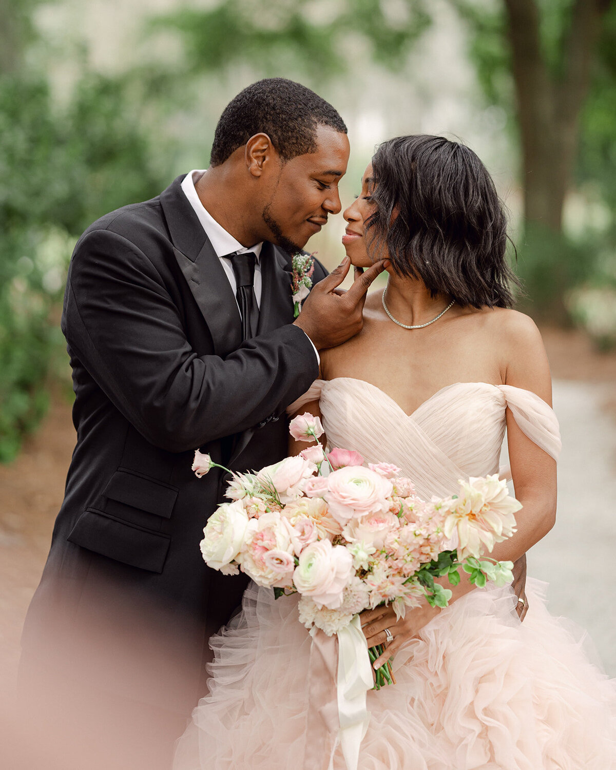 Groom leans in to kiss his bride who is wearing a light pink tulle wedding dress.