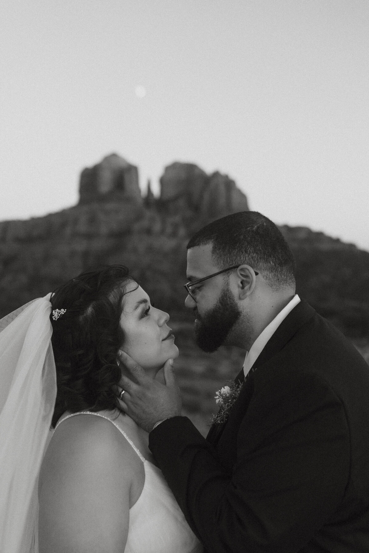 Black and white photo of someone reaching towards their partner's cheek as they lean in to kiss 