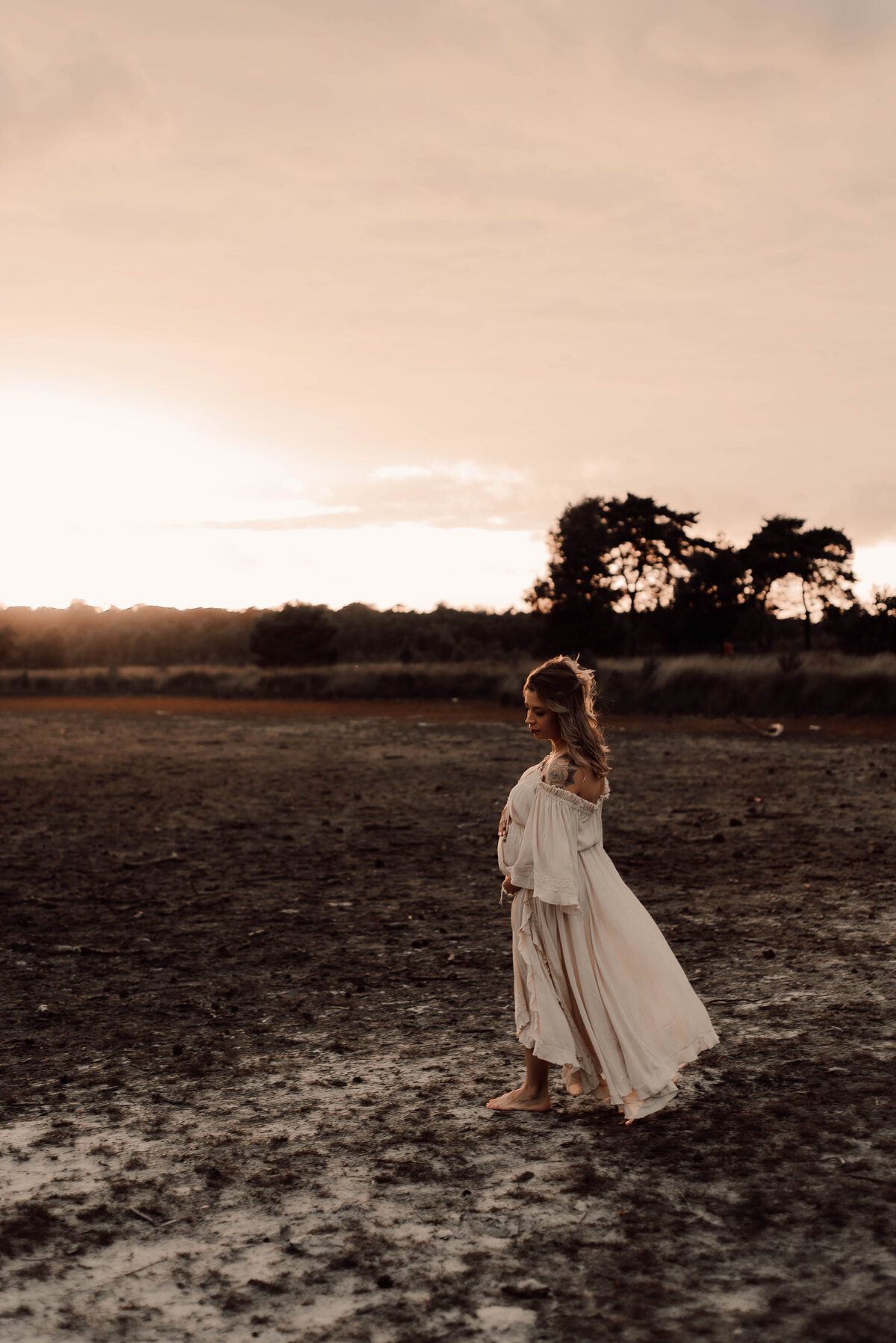Zwangere vrouw in jurk poseert voor zwangerschapsshoot tijdens zonsondergang op de Kalmthoutse Heide