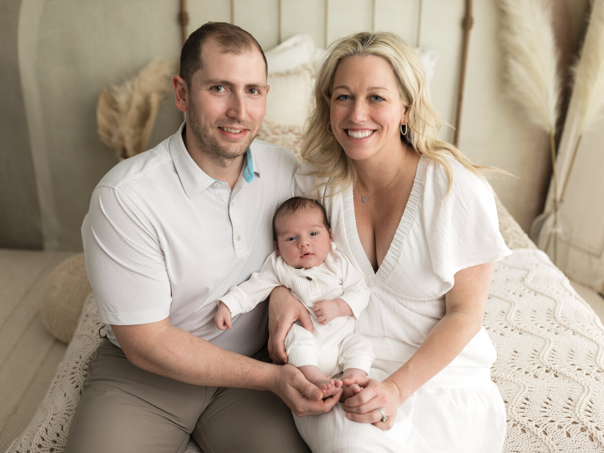 mom and dad holding newborn baby boy in white onesie for studio lifestyle session 