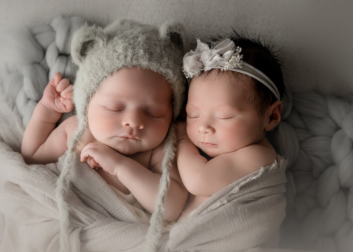 Twin Newborn baby boy and girl cuddle while sleeping in a bear cap and bow headband
