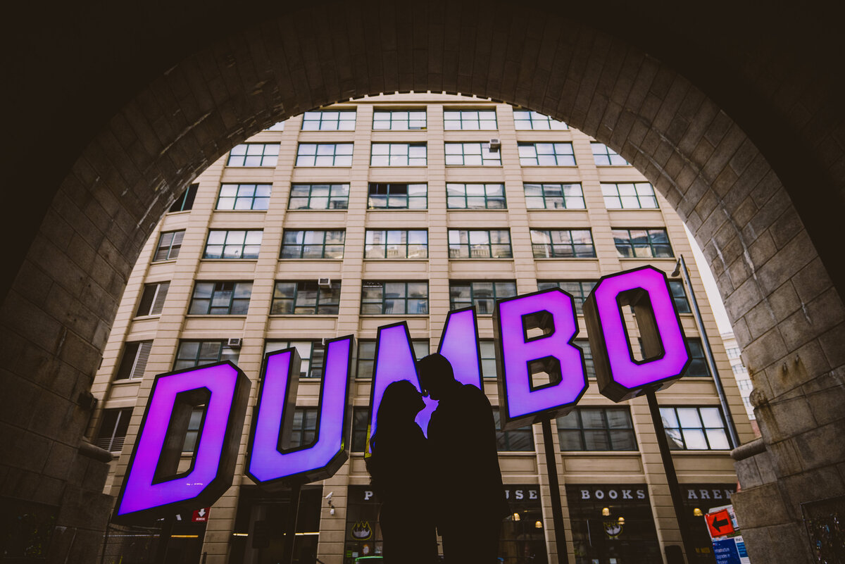 A silhouette of a couple in the middle of an led sign that says dumbo in the tunnel at dumbo brooklyn