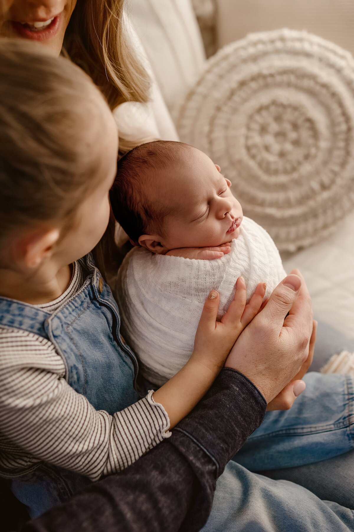 A family gathers on their bed, big sister gently touching her baby brother’s nose in this sweet newborn family picture.
