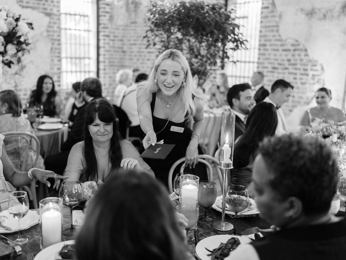 A server gracefully interacts with guests at a beautifully arranged wedding dinner, providing attentive service amidst joyful conversations and elegant dining decor.