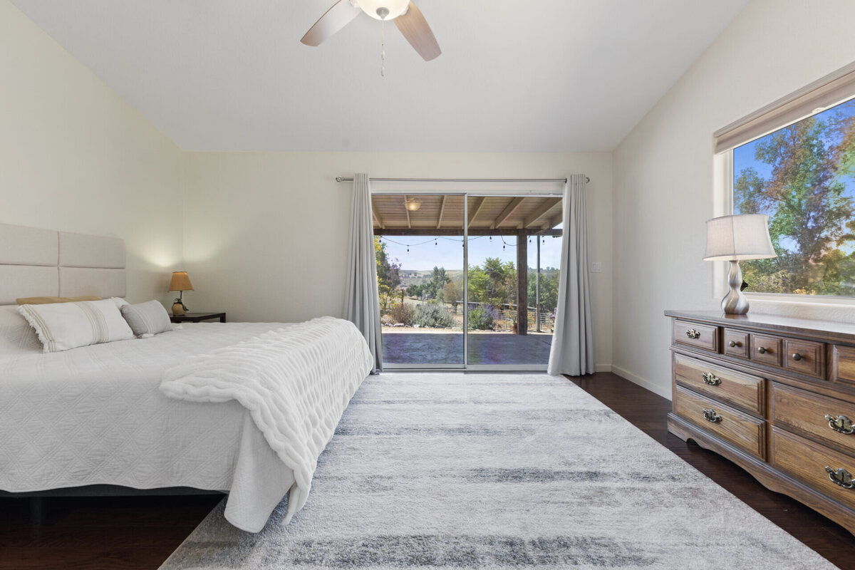 Primary bedroom with bed, dressers and a view through the sliding doors to the front yard. Real Estate home in Ramona.