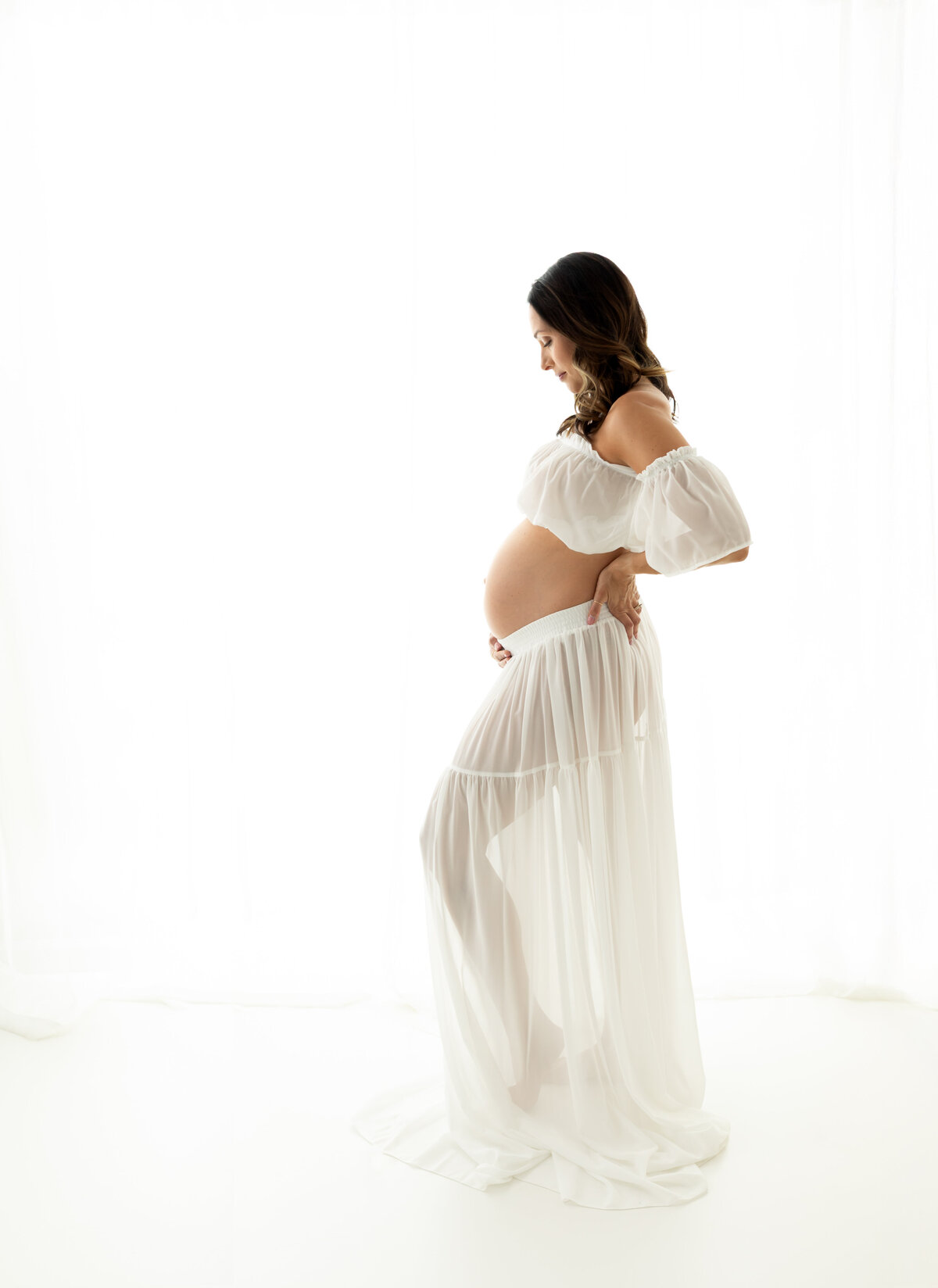 pregnant mother in white two piece maternity gown holding baby bump for maternity photoshoot