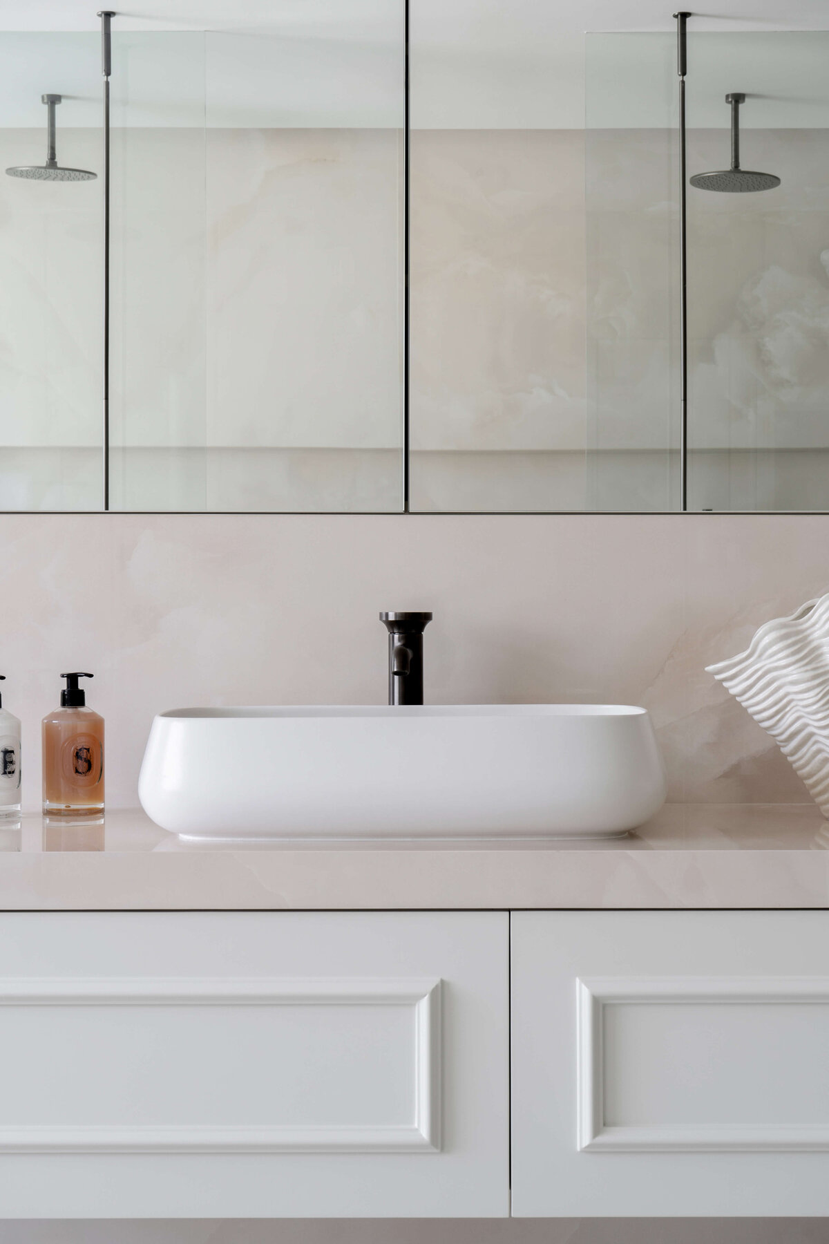 Close-up detail of a sink in the primary bathroom. The room is airy and light. The sink hardware is a stark black and contrasts the white bowl.