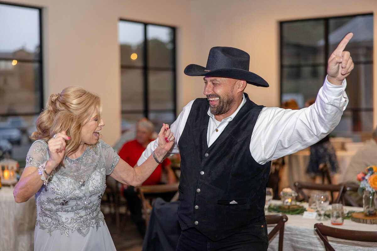 guests dance at wedding reception man in black vest and cowboy hat