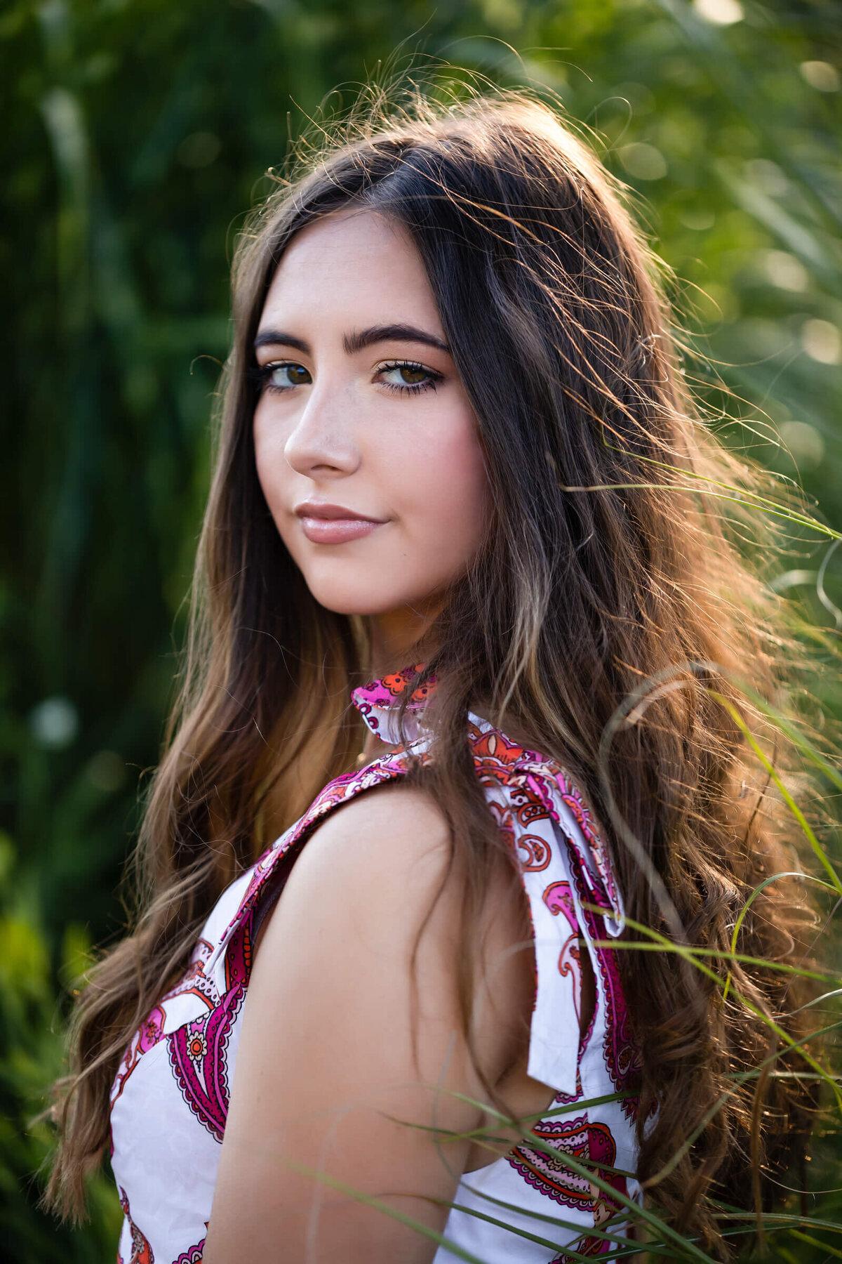 A close up headshot of a high school senior girl with long brunette hair looks over her shoulder at the camera. Captured by Springfield senior photographer Dynae Levingston.