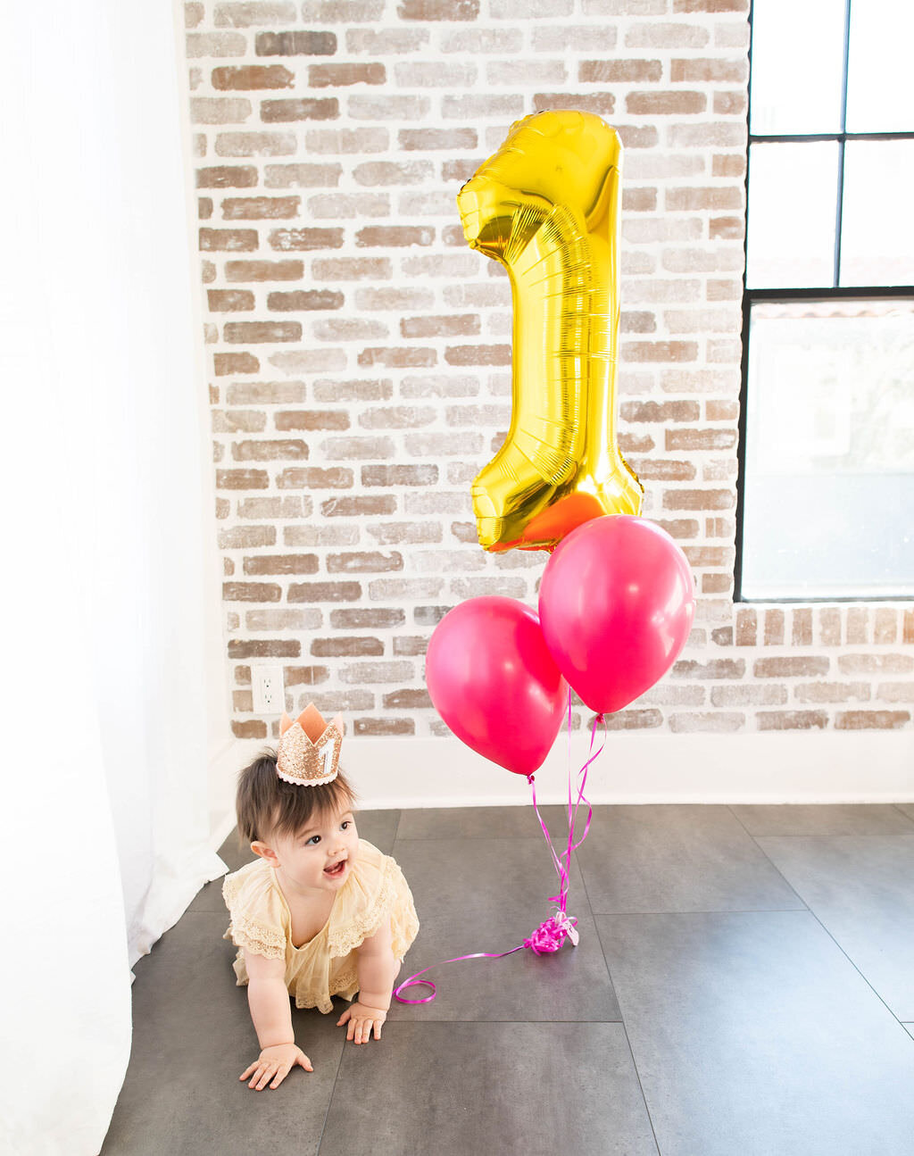 A baby with "1" and pink balloons next to her.