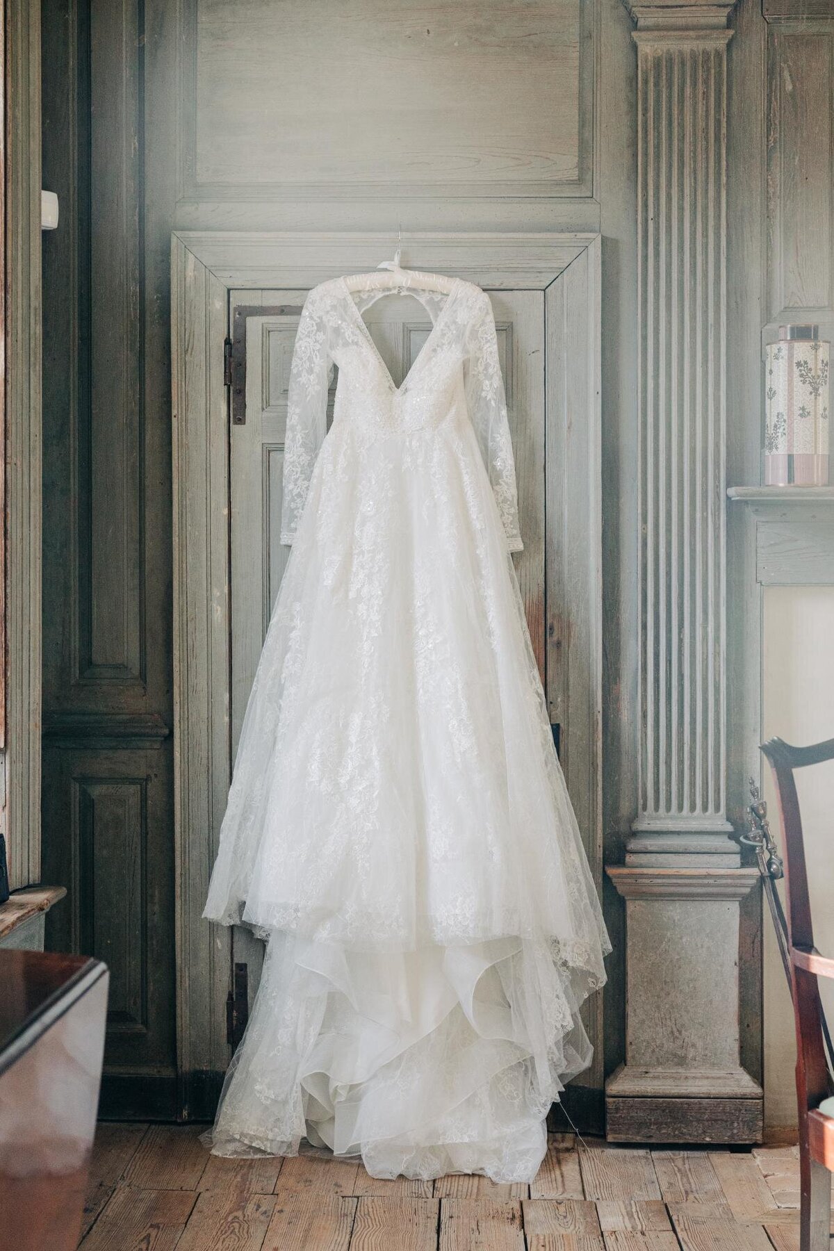 An elegant wedding dress hanging on a vintage wooden door in a rustic room.