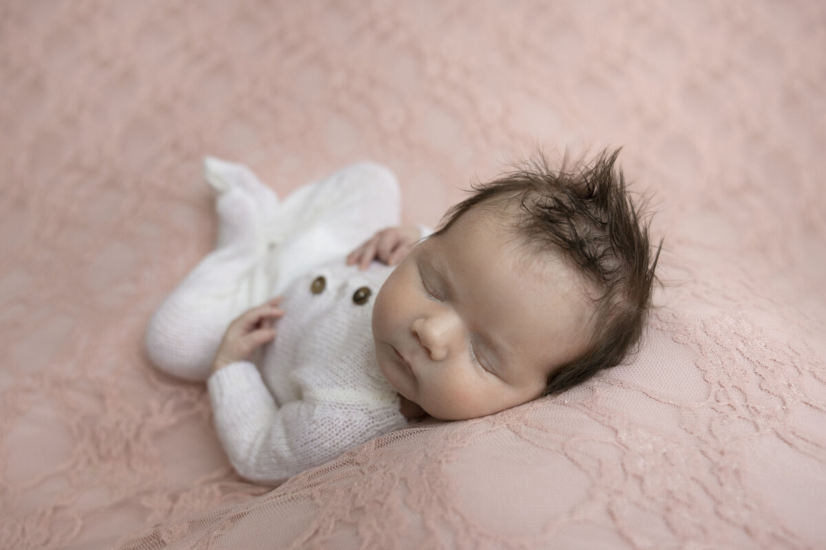 Infant lays on back on a floral pink background wearing a white button up sleeper.