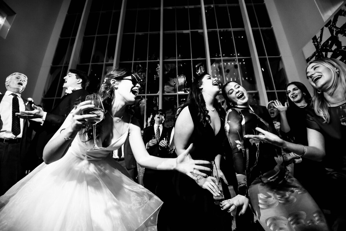 Black and white image of bride wearing sunglasses singing with best friends at the Mint Museum Uptown by Charlotte wedding photographers DeLong Photography