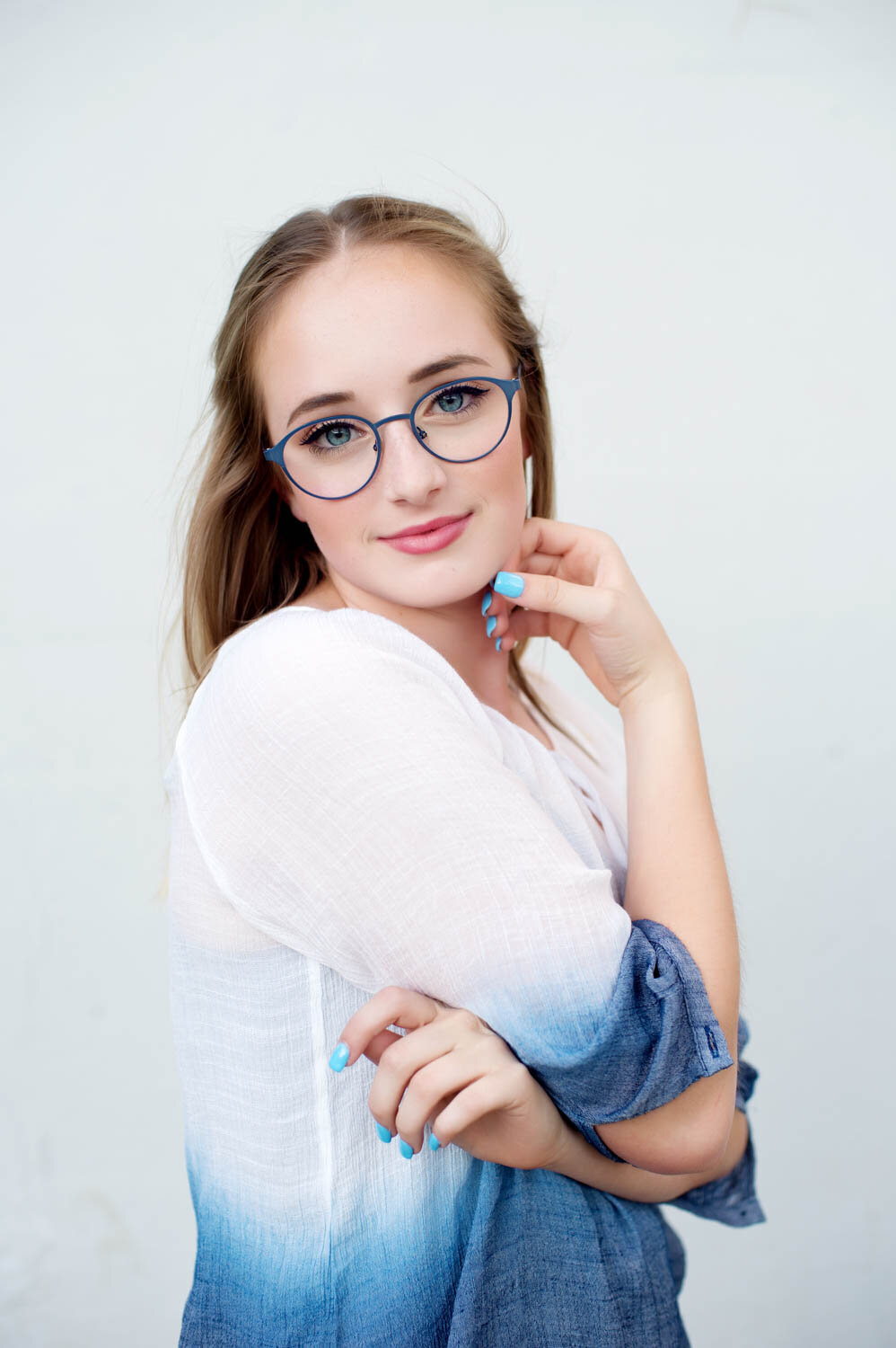 Professional head shot of young woman with colorful blue glasses and an ombre blue and white shirt.