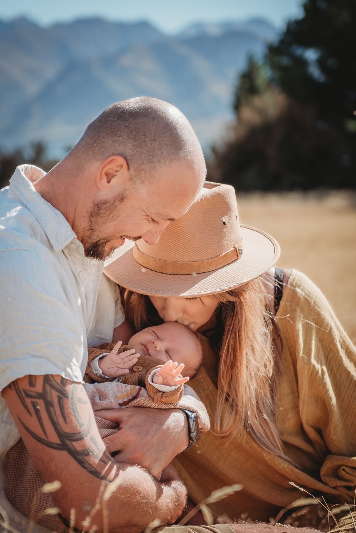 parents sitting down and mum kissing baby on the head while posing for a newborn photography session