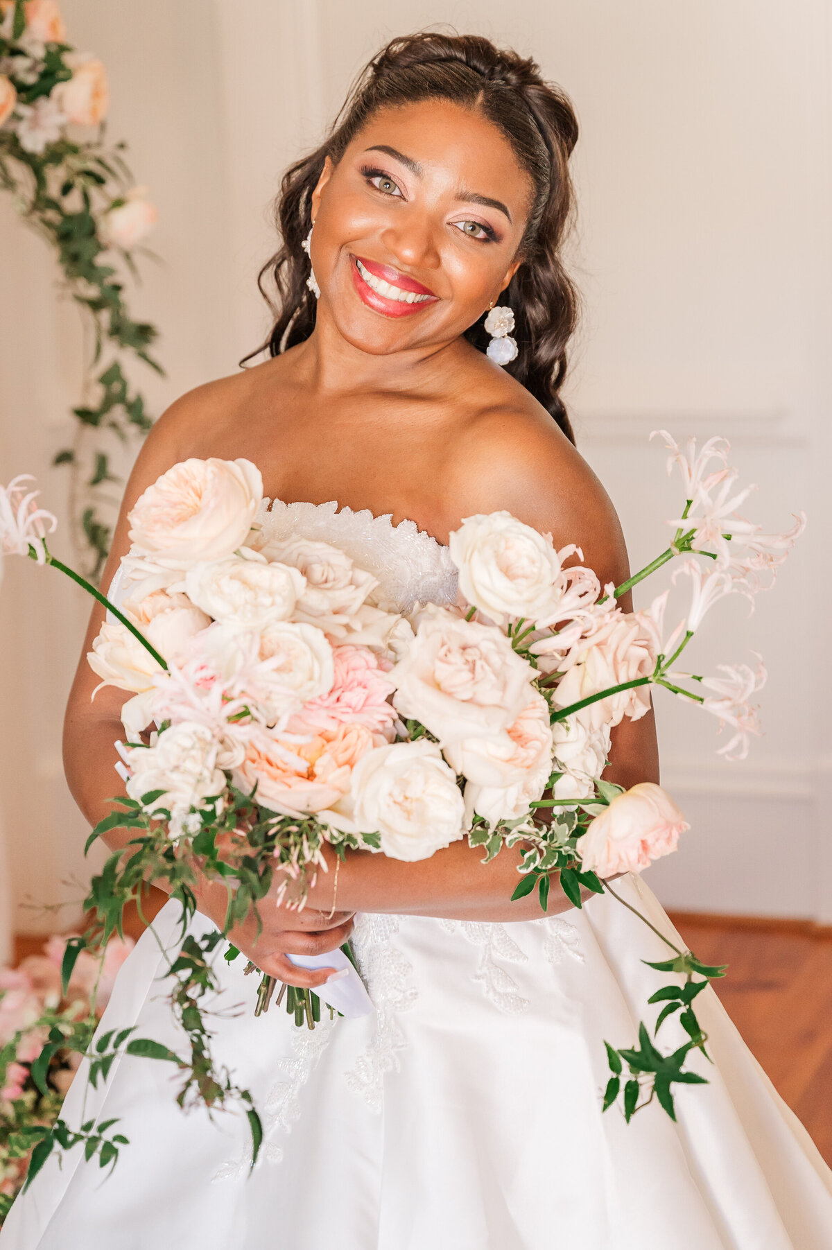 A glowing African American bride during her bridal portrait session at Donovan Manor while holding pastel pink and white flowers during the springtime by JoLynn Photography