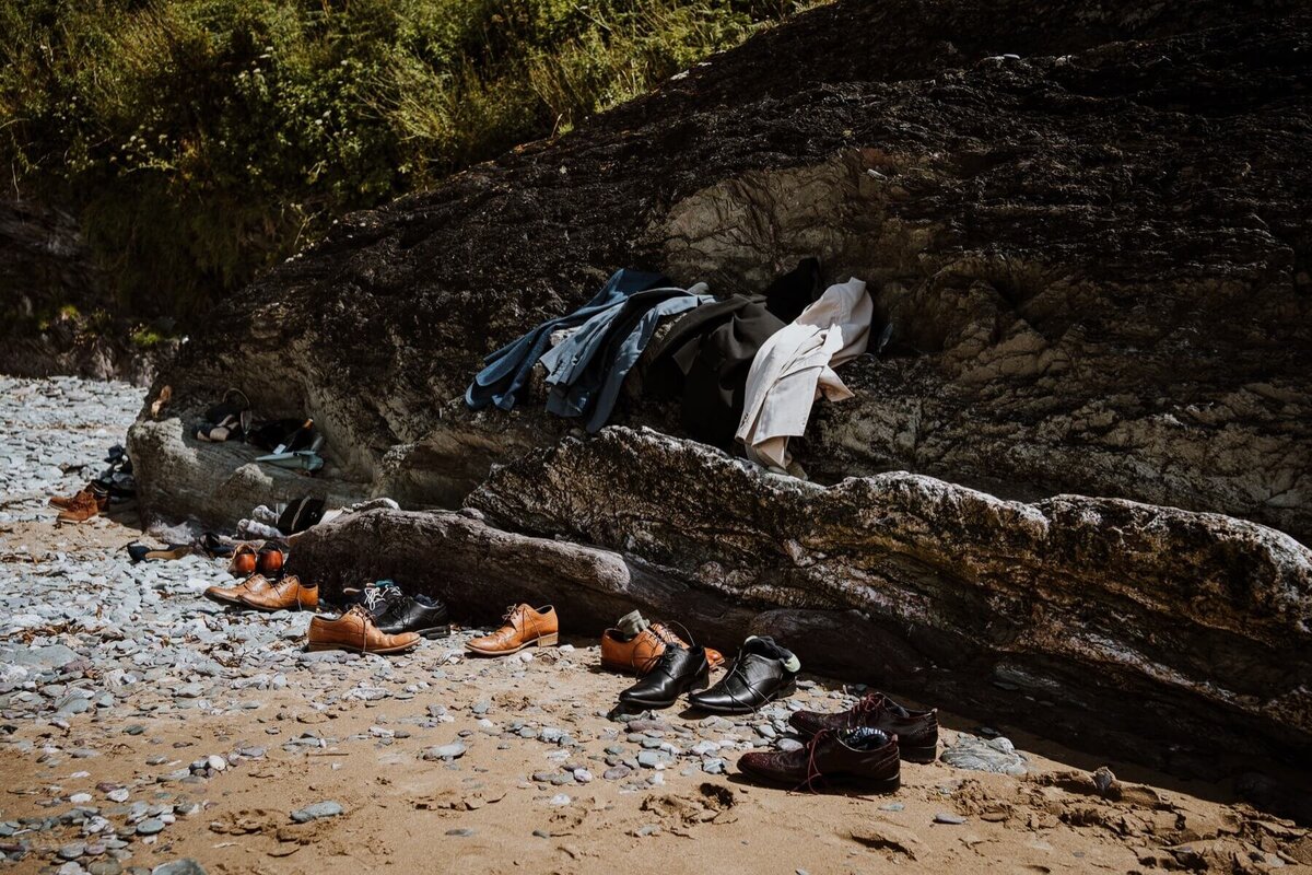 A pile of clothes and shoes on some rocks at a beach