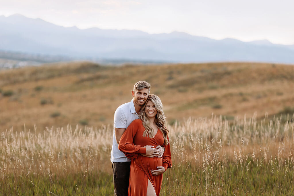 gorgeous couple embracing as the pregnant mom holds her bump with the flat irons in the backdrop of their denver maternity photos