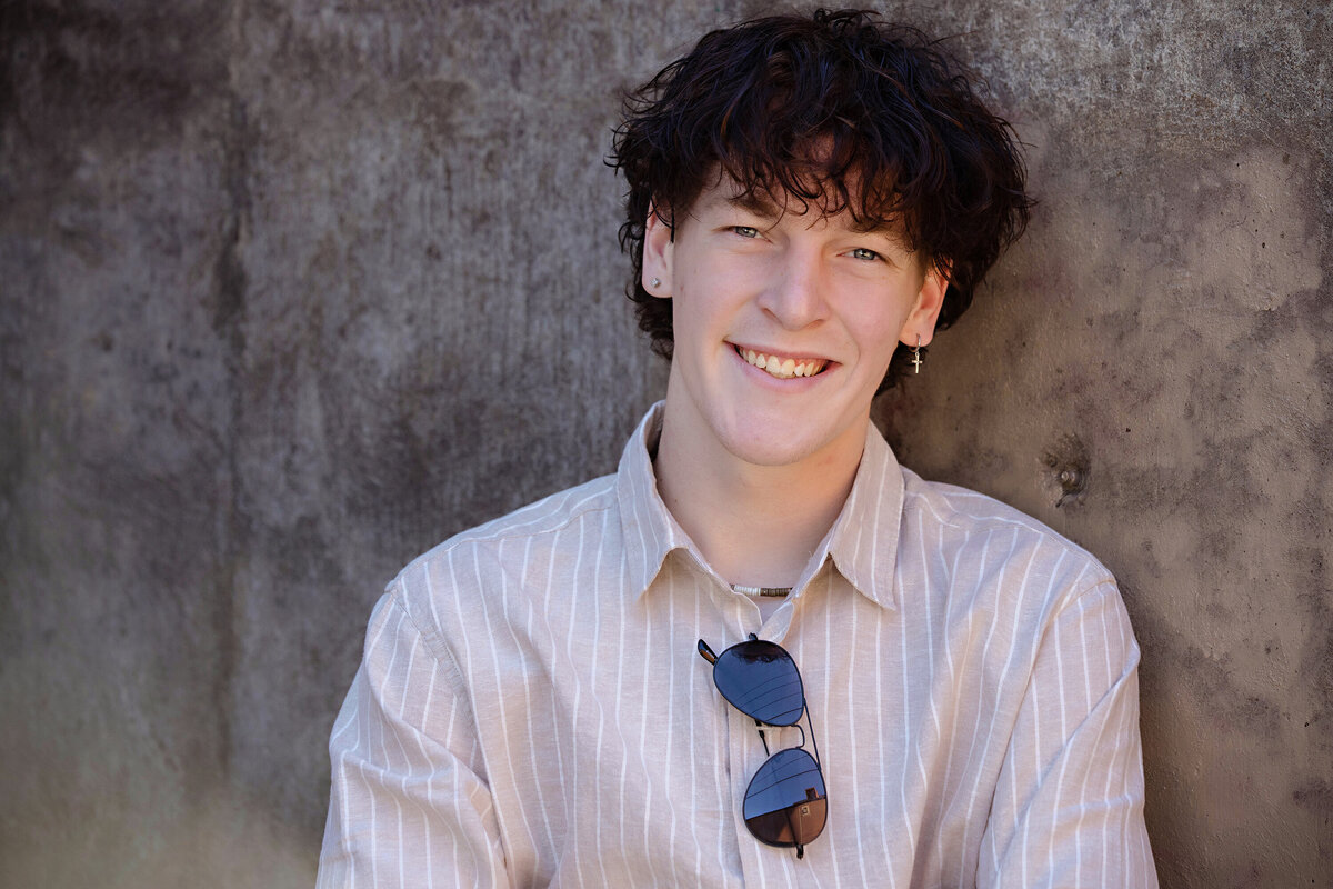 Close-up of senior wearing sunglasses and a vertical stripe shirt, captured in spring by Charlotte photographer at Camp North End.