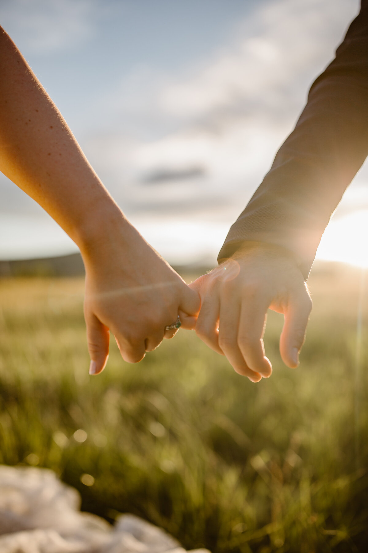 Close-up of a couple holding hands with pinkies intertwined during golden hour at Shupe Homestead, with sunlight highlighting the bride’s engagement ring.