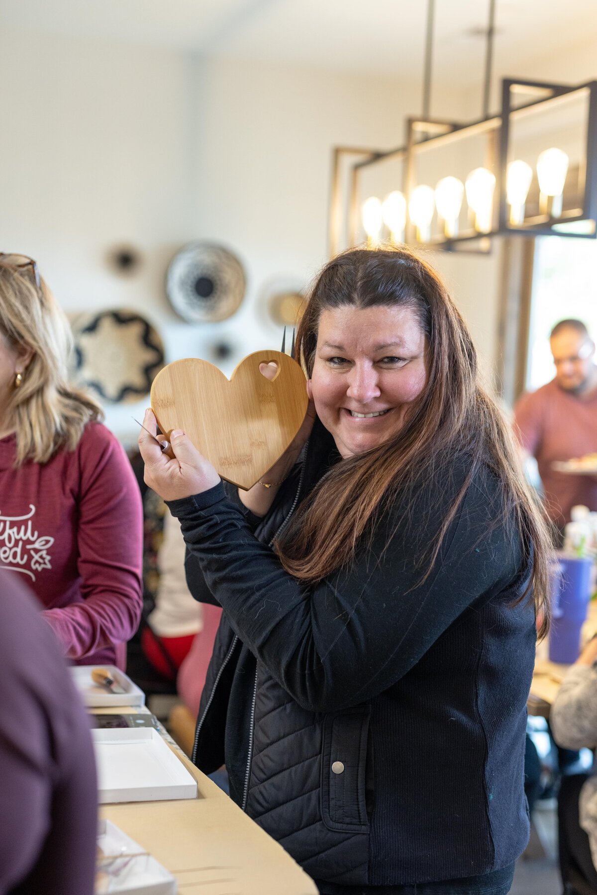 woman holding wooden tray with a heart on it smiling at camera