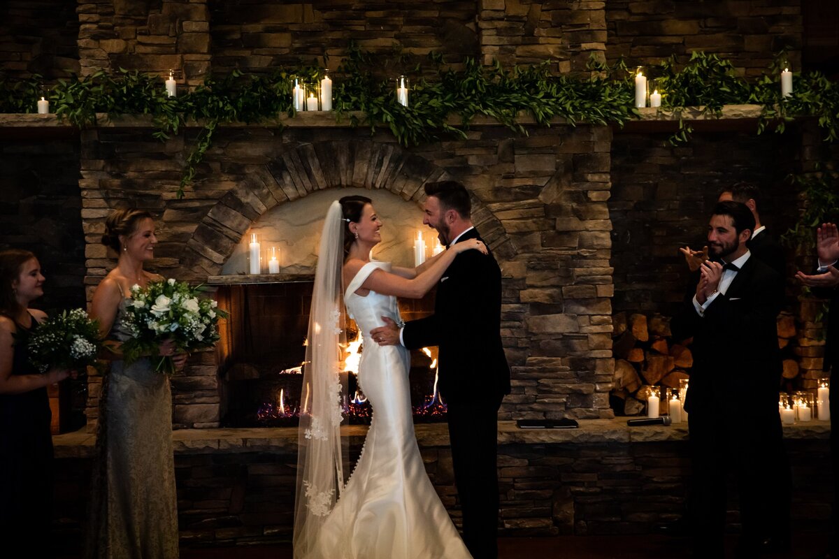 Bride and groom during their wedding ceremony in front of a candle lit fireplace with greenery and white flowers at Spruce Mountain Ranch.