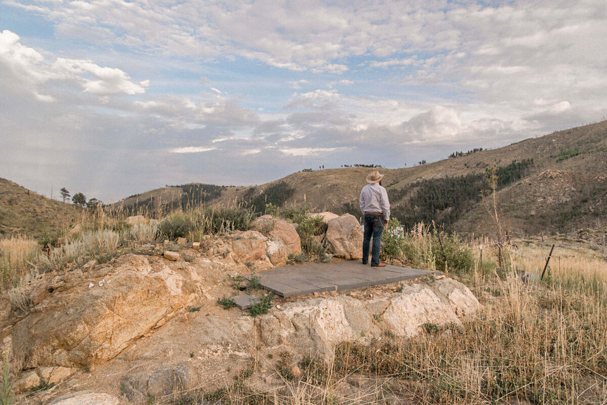 The groom stands with his back to the camera, waiting for his bride, in front of a majestic mountain vista