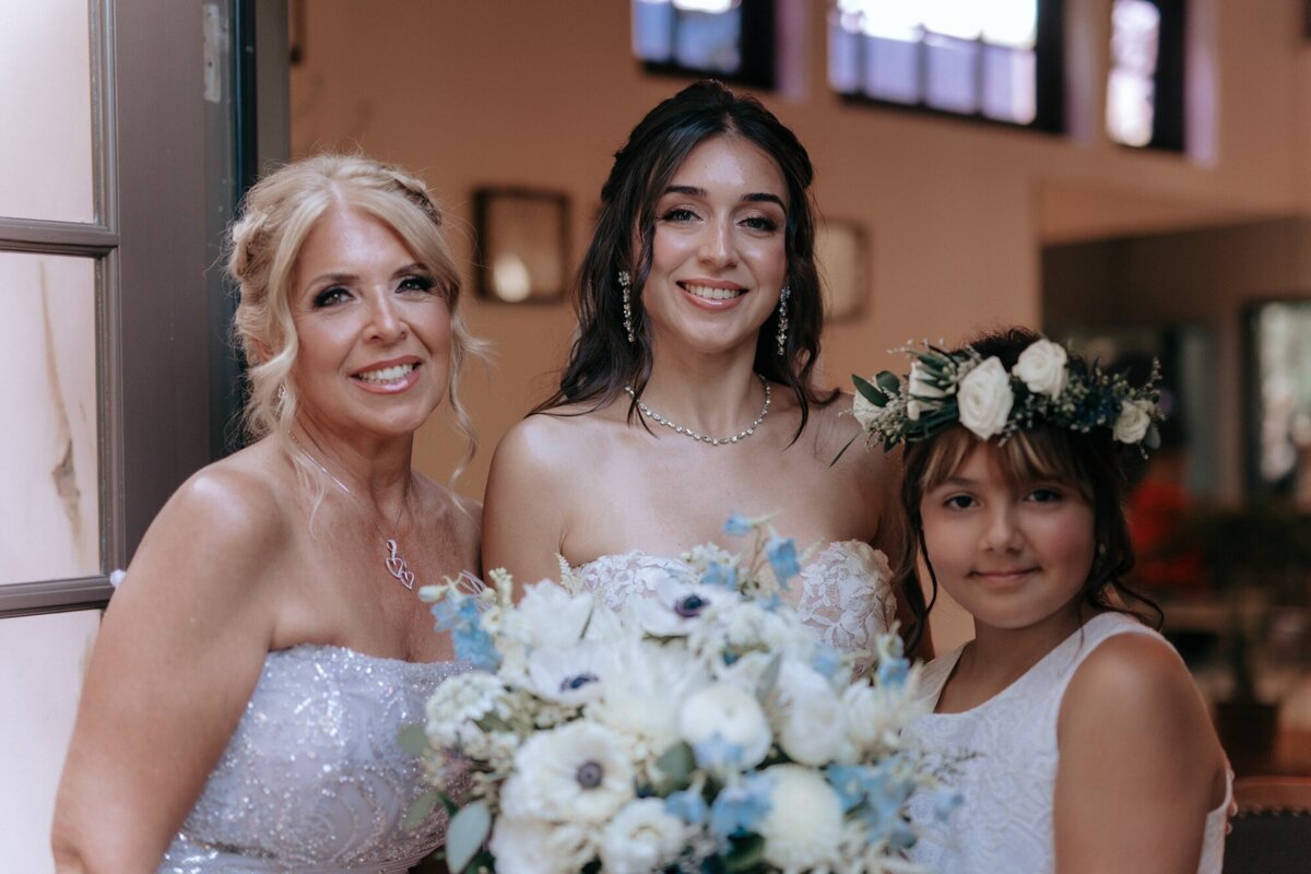 Bride with a woman and girl from the wedding party holding her bouquet.