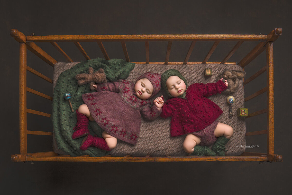 Twins sleeping and holding hands in a vintage wooden crib.