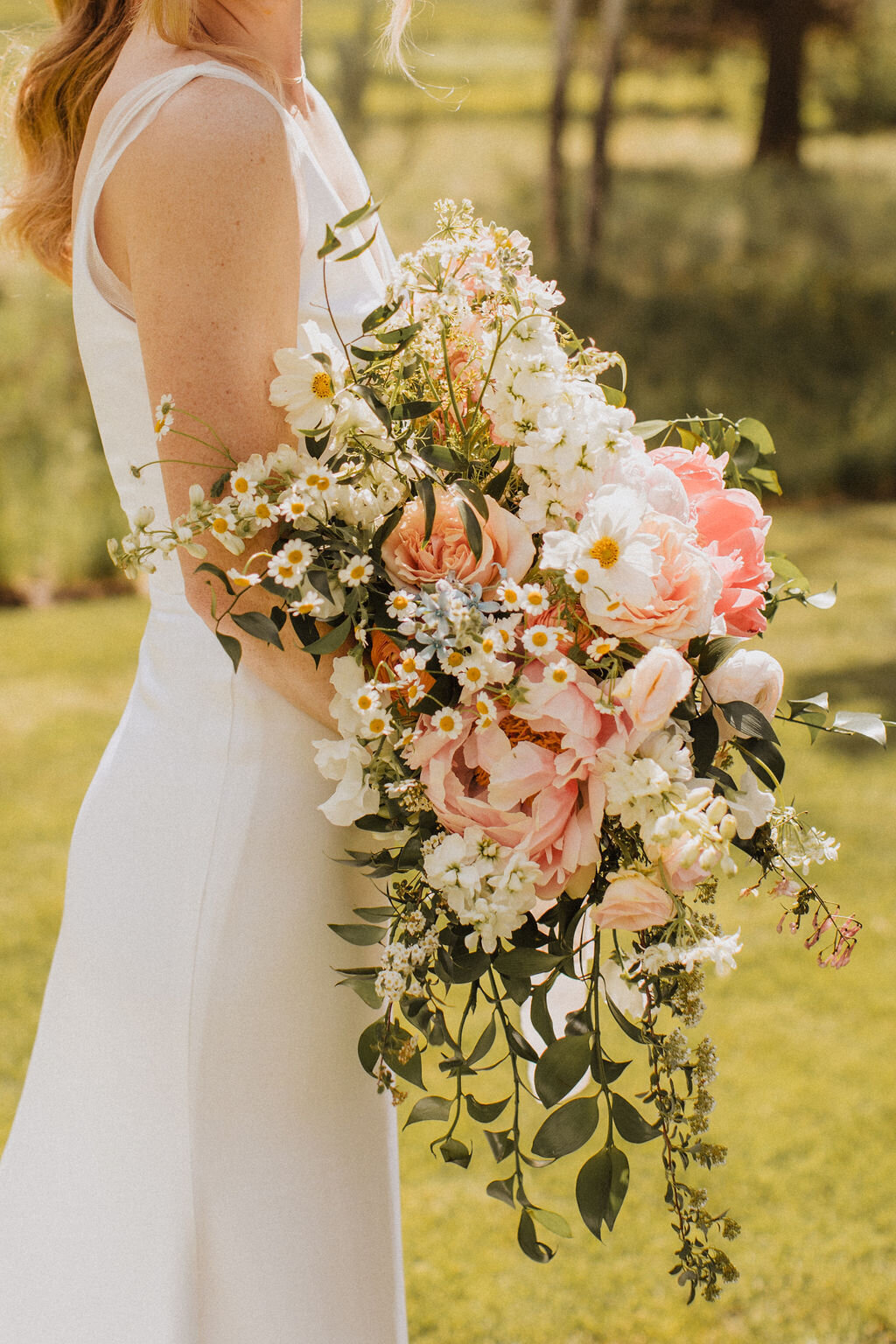 Bride holding cascading bouquet of peony, chamomile, cosmos, roses, ranunculus and spirea
