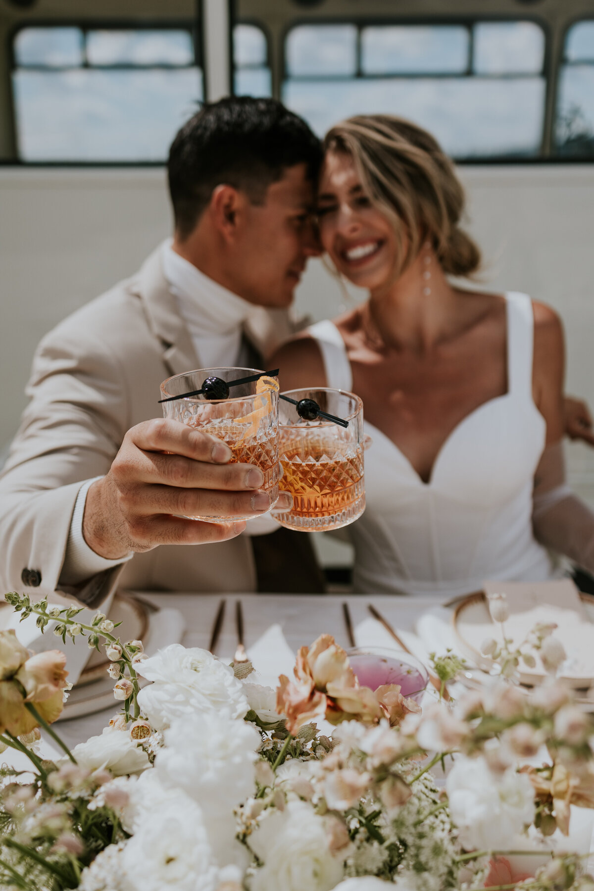Bride and groom laugh while toasting together.