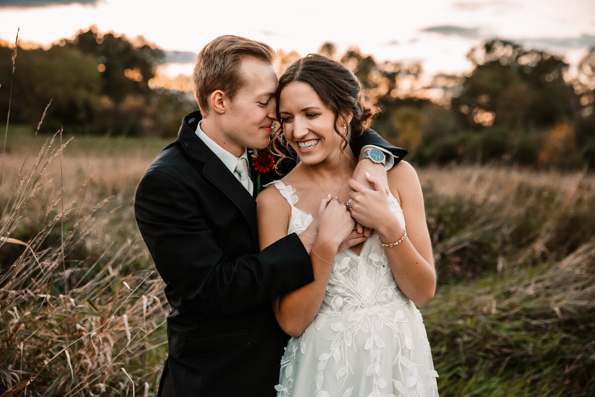groom holds brides shoulders at sunset in a field