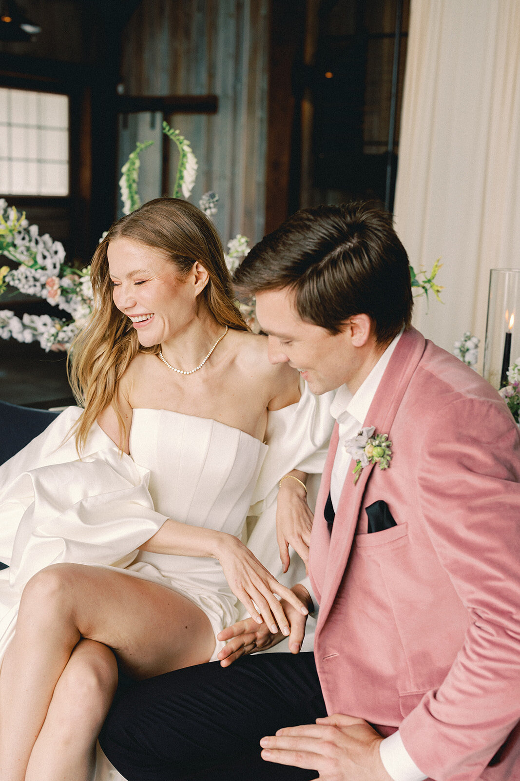 Groom in a pink jacket holding bride's hand and laughing
