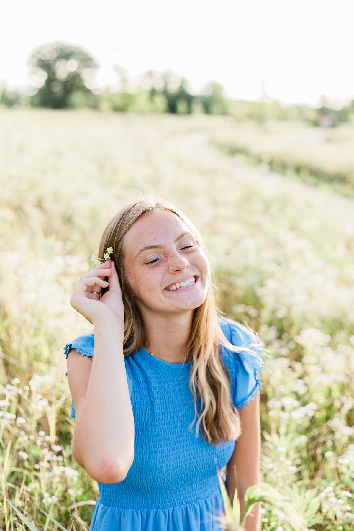 girl sitting in a field putting flowers in her hair and laughing