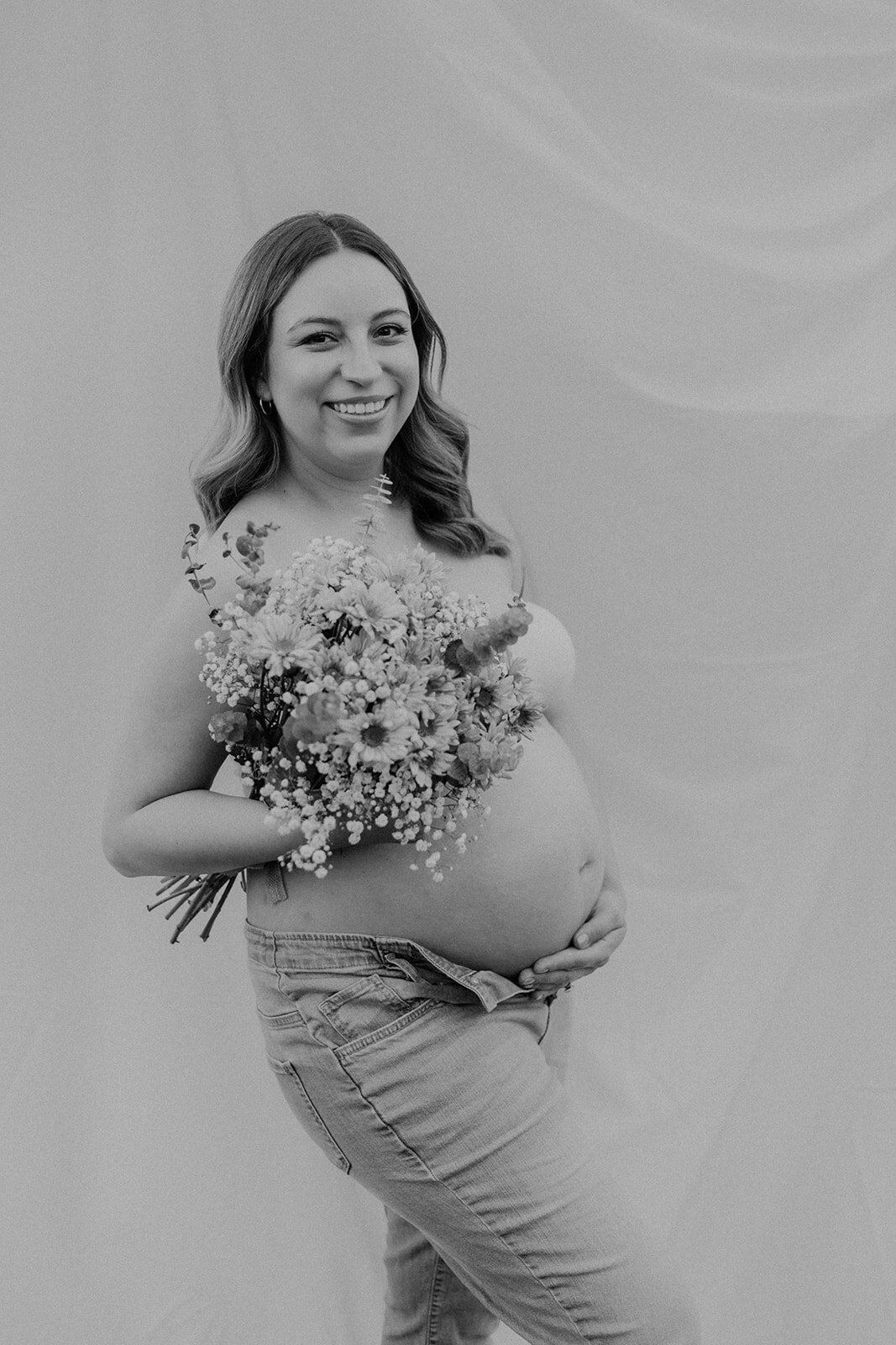 A pregnant woman smiles while holding flowers