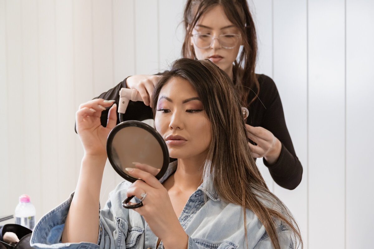 Asian Lady looking in Hand Mirror while someone else does her hair.