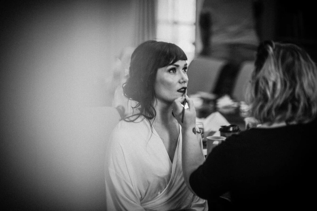 A woman putting makeup on a bride.