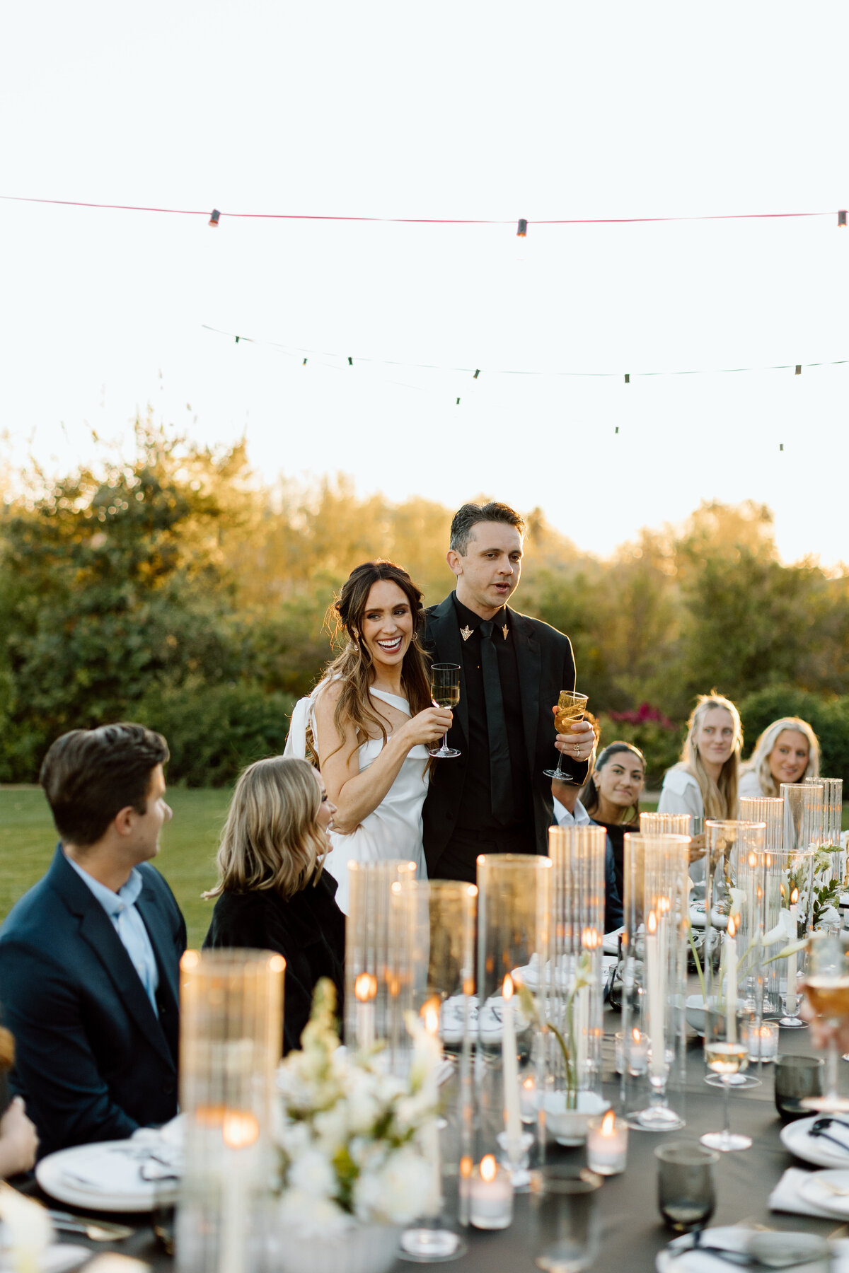 bride and groom giving a toast during an elegant golfcourse wedding dinner, with glowing candlelight and joyful guests